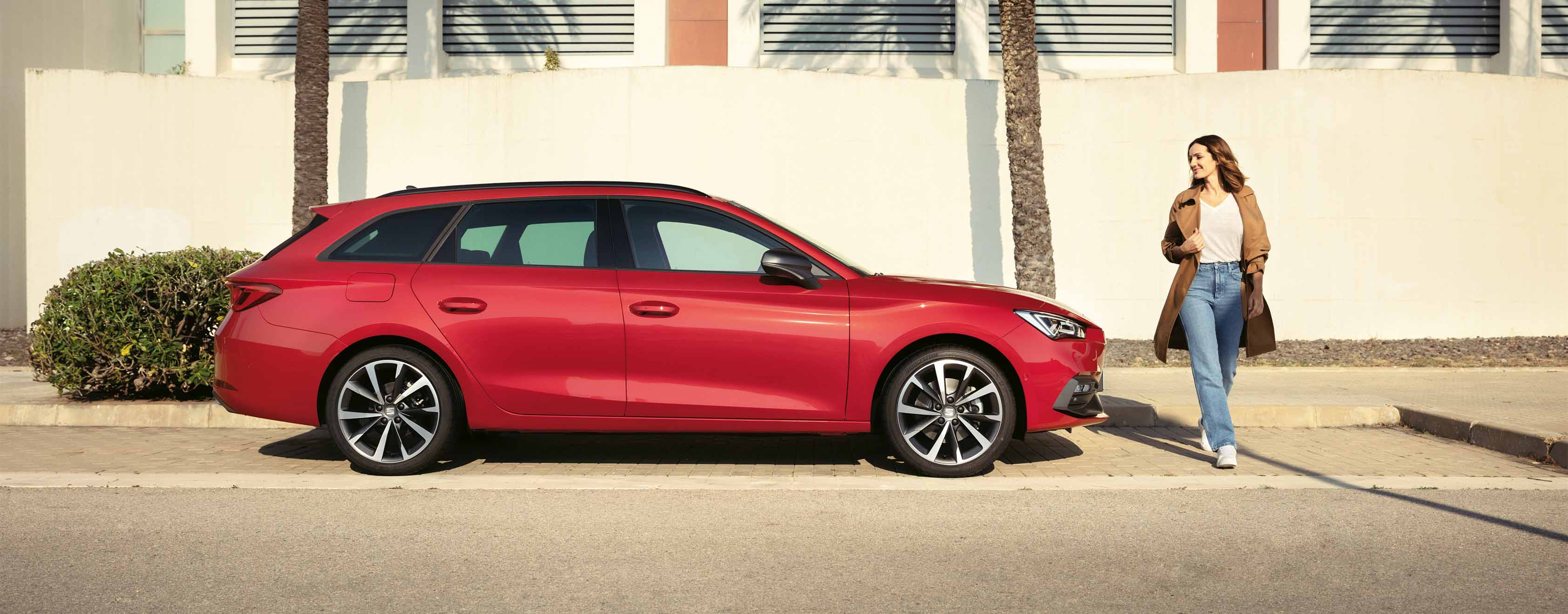 Side view of a red SEAT Leon Sportstourer 2024 in a car park, woman looking at the front