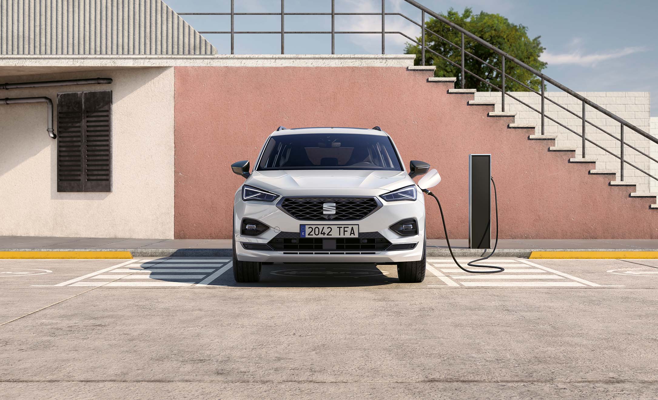 Front view of white SEAT Tarraco 2024 suv charging against pink wall in a car park