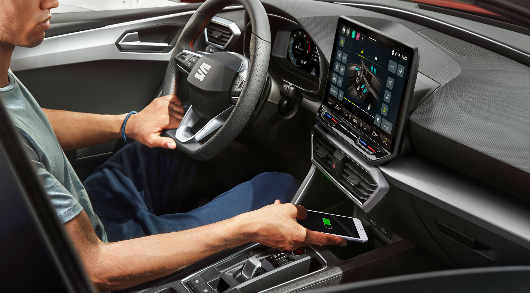 man holding seat leon 2024 steering wheel while placing phone to charge in refrigerated box, infotainment system screen on.