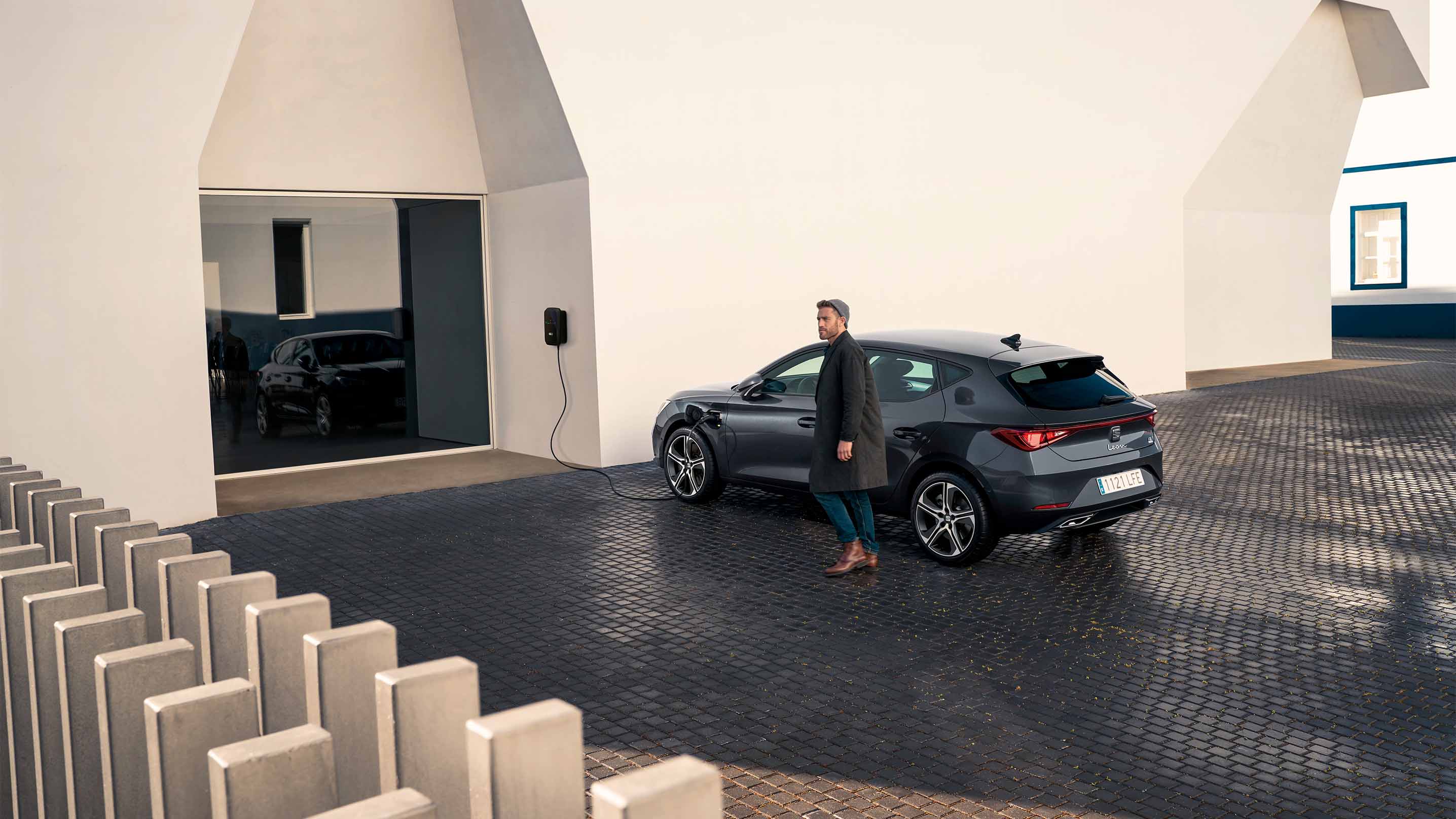 SEAT León vehículo eléctrico híbrido enchufable aparcado y cargando en el exterior de un moderno edificio, ideal para conductores urbanos ecológicos