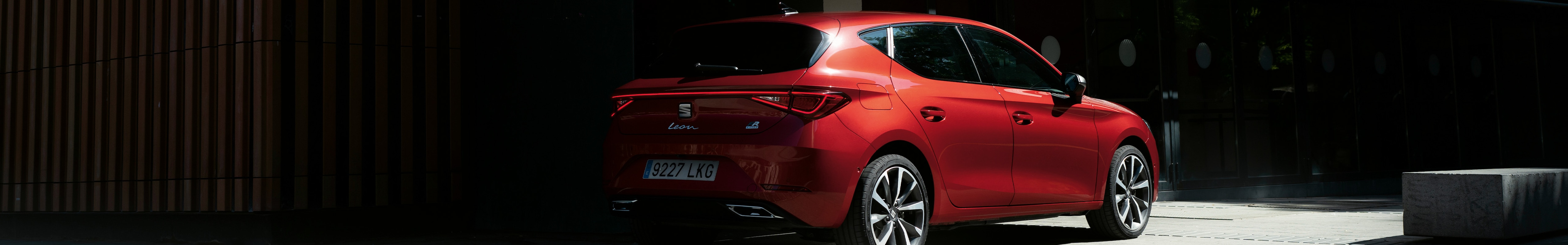 coche micro híbrido eléctrico seat leon sporstourer rojo aparcado a la sombra de un edificio