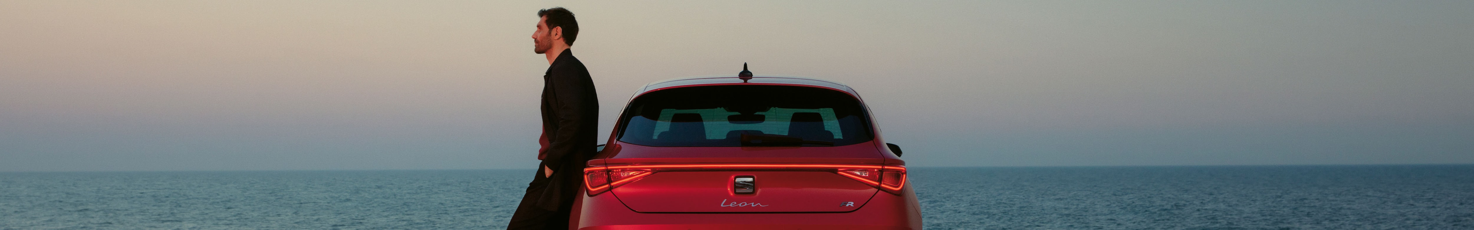 coche seat híbrido enchufable leon rojo, vista de faros traseros, al atardecer junto al mar