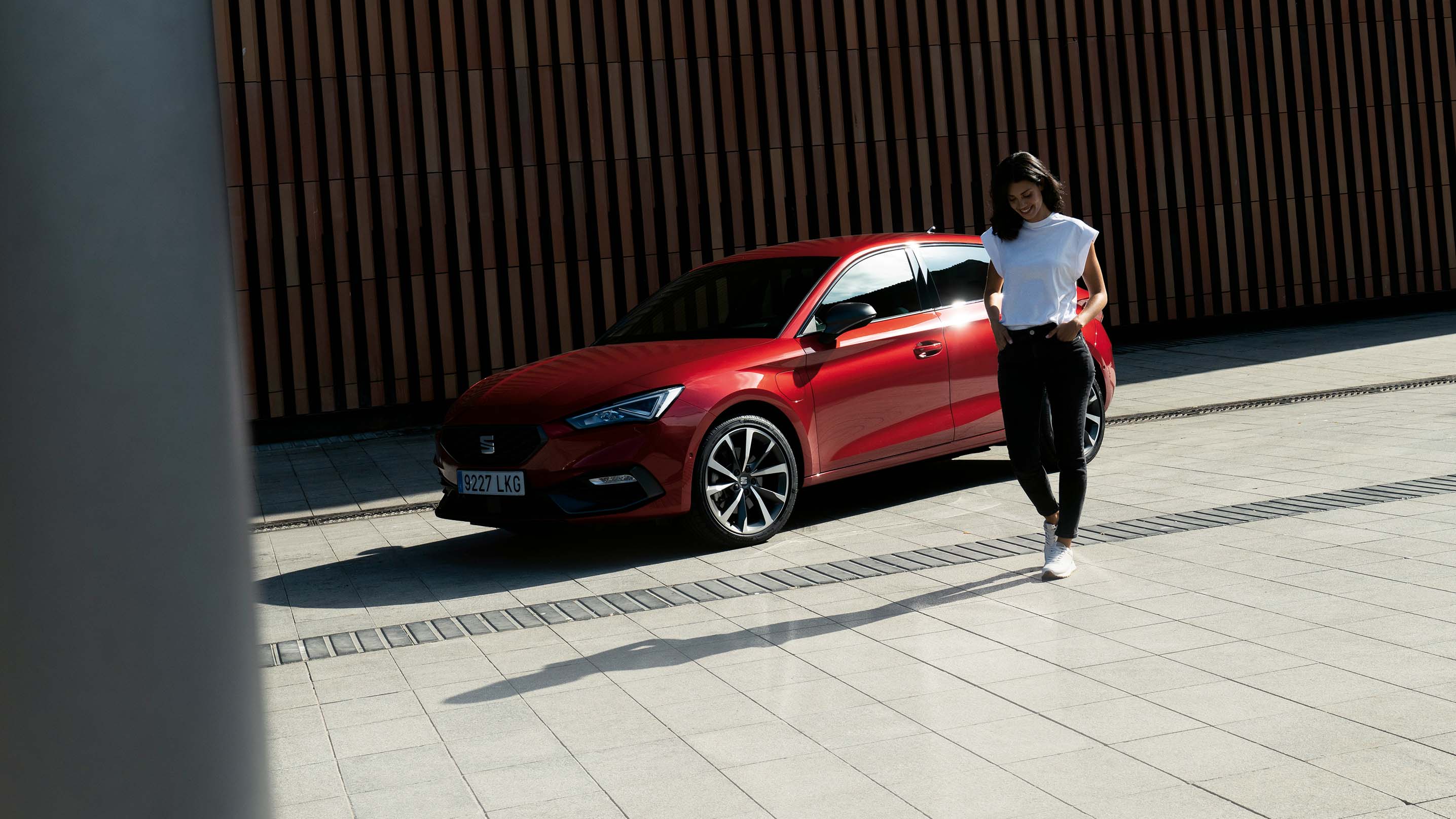 Vehículo híbrido SEAT León rojo aparcado a la sombra junto a un edificio